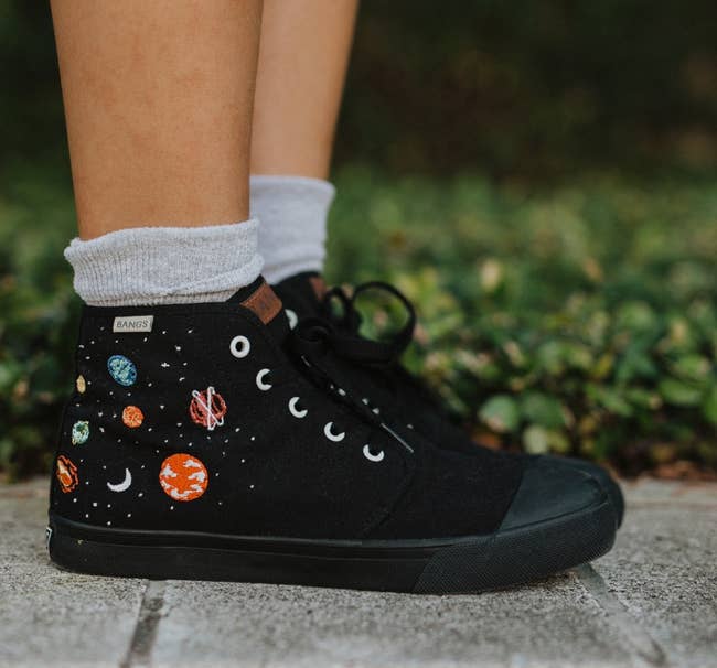 a model wearing black high-top canvas sneakers with planetary embroidery 