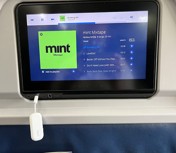 reviewer photo of the AirFly Pro plugged into the headphone jack on the back of a plane seat