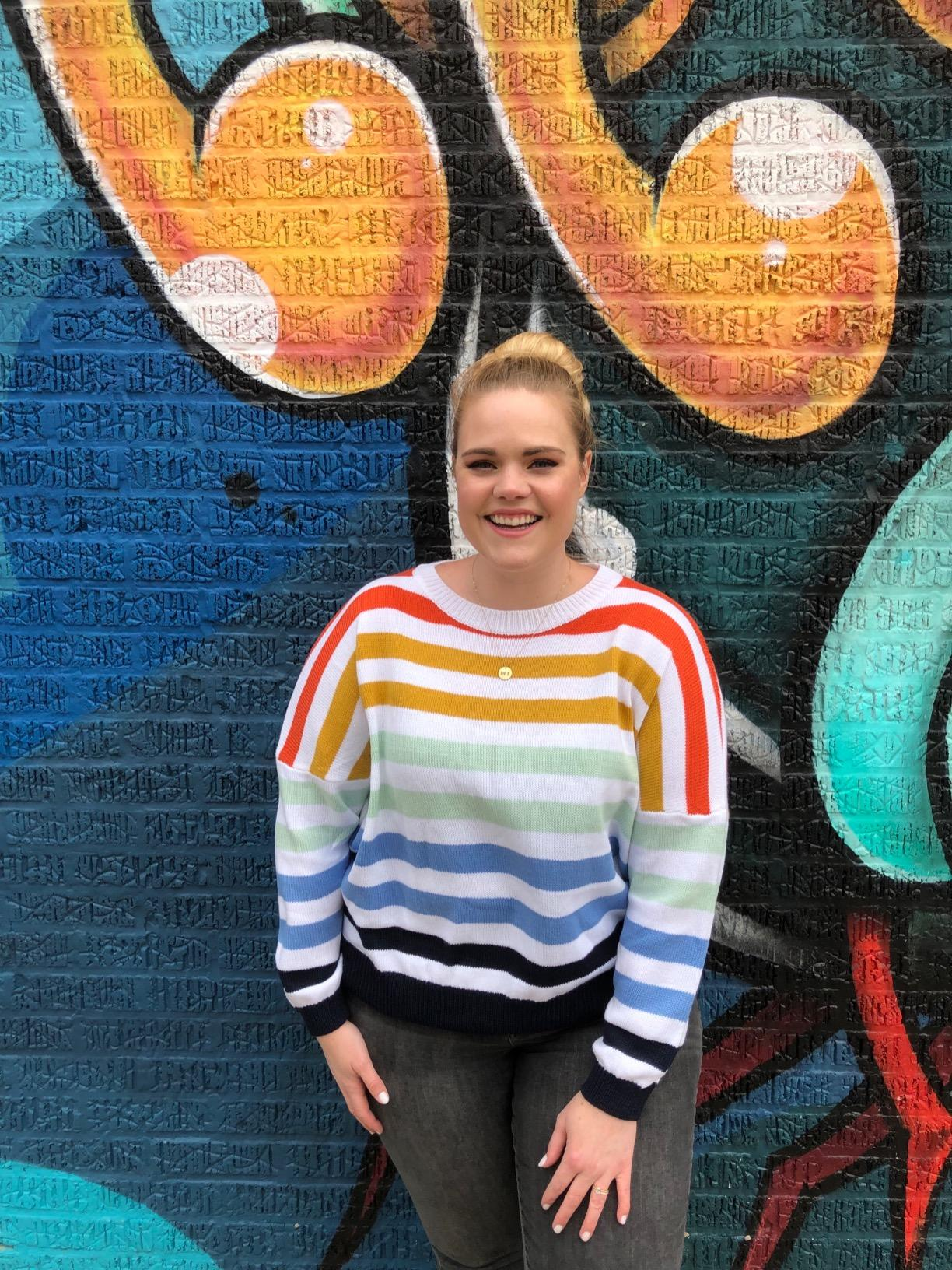 a reviewer wearing the same sweater featuring a white background and rainbow stripes