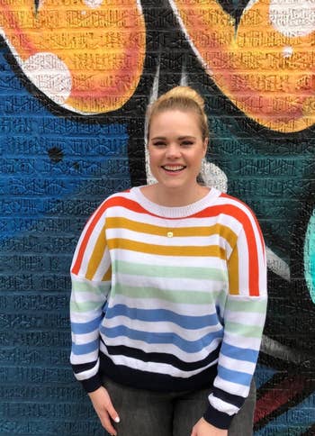 a reviewer wearing the same sweater featuring a white background and rainbow stripes 