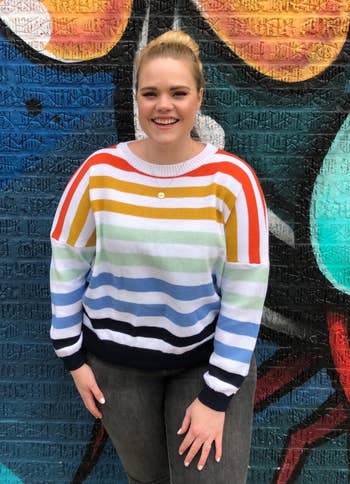 a reviewer wearing the same sweater featuring a white background and rainbow stripes