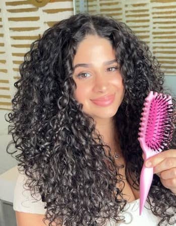 Person with curly hairsbreadth  smiling, holding a pinkish  brush, suitable for styling curls
