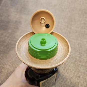 Close-up of a manus holding a vessel with an unfastened flip-top lid, revealing the spout and interior seal, suggesting easiness of usage for dispensing
