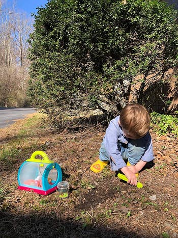 Child plays with bug catching kit in dirt next to a backpack and jar, outdoor setting