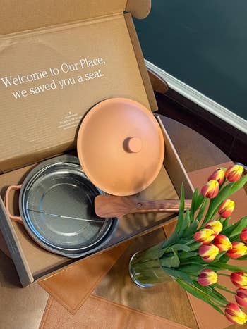 Our Place cookware acceptable   with a lid and strainer successful  a container  adjacent  to a vase of tulips connected  a table. Box connection   reads 