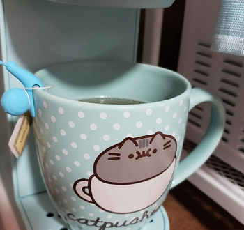 reviewer photo of the blue snail holding a tea bag on the rim of a mug