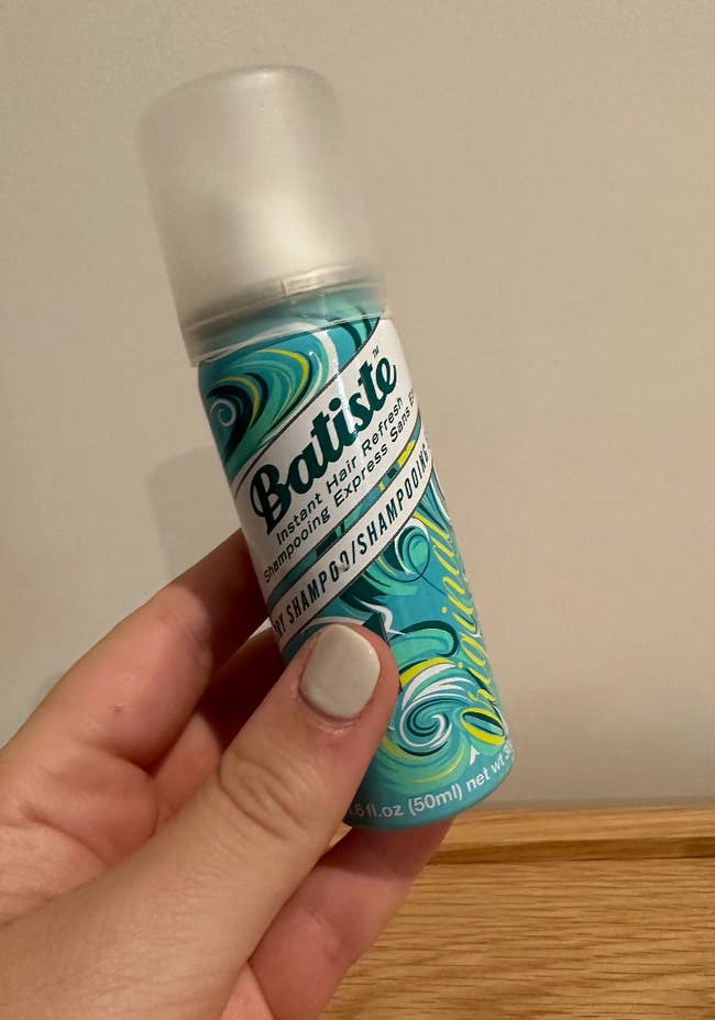 a BuzzFeed writer holding a travel sized bottle of dry shampoo