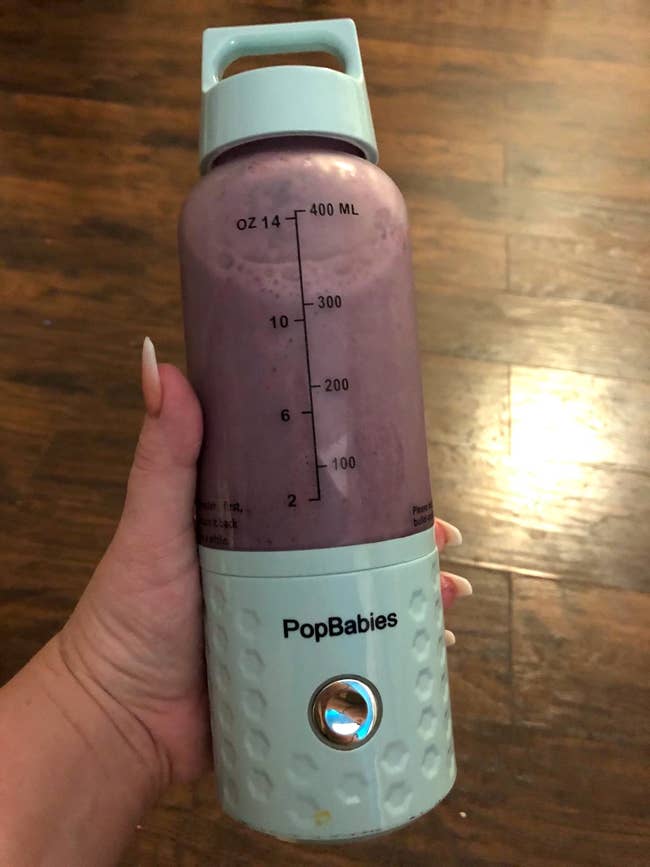 reviewer holding the blue popbabies portable blender and showing the measurements on the side
