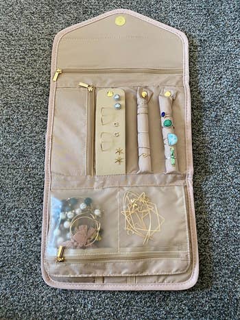 Jewelry organizer displaying earrings, necklaces, and rings. The case is open with compartments for various accessories, suitable for travel use