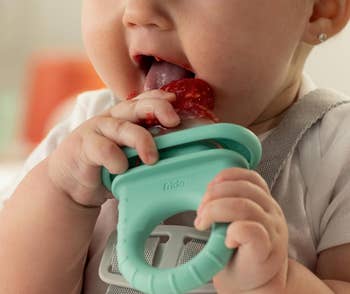 Baby using a teal feeder to eat fruit