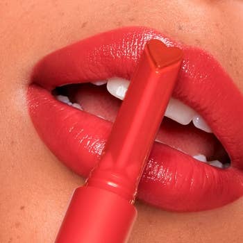 Close-up of lips, showing off juicy, shiny, and peachy pink color and the heart-shaped gloss stick