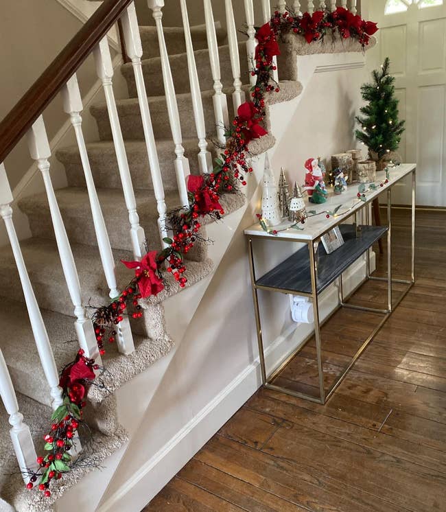 reviewer photo of the red poinsettia and berry garland wrapped around their staircase railing