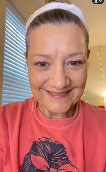 Person wearing a pinkish T-shirt with a graphic design, smiling astatine the camera. They person a achromatic headband and are indoors with model blinds down them