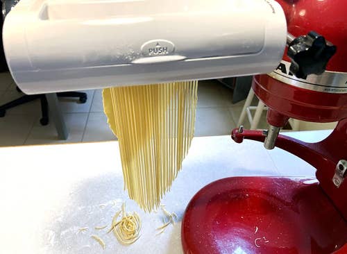 reviewers pasta maker attachment on a stand mixer with fresh spaghetti noodles being made