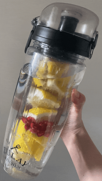 BuzzFeeder holding the water bottle, which has a center compartment filled with sliced fruit