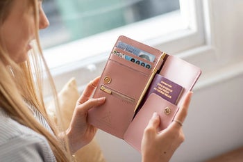 model holding open the pink travel wallet, which has cards and a passport inside