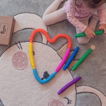 a heart made out of multicolored pop tube sensory toys with a child model holding a green tube