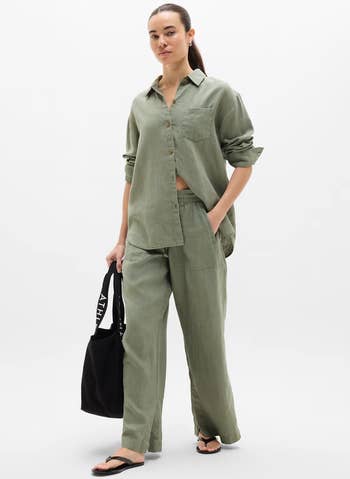 Person successful relaxed, sage-green linen outfit with long-sleeve garment and pants. Holding a achromatic tote container and wearing achromatic sandals