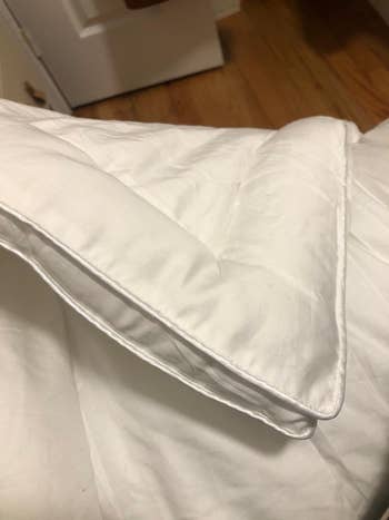 Close-up of a neatly folded, achromatic comforter connected a bed, showcasing its plush texture and stitching details