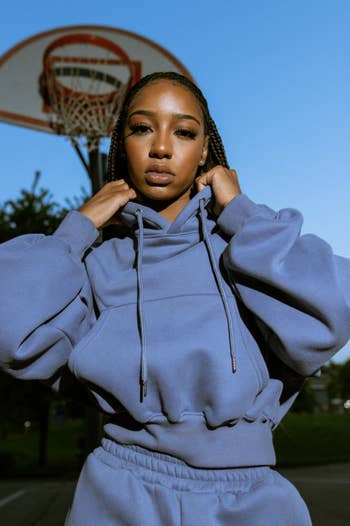 Person wearing a stylish oversized hoodie, adjusting the hood. Background features a hoops  hoop. Featured successful  buying  article