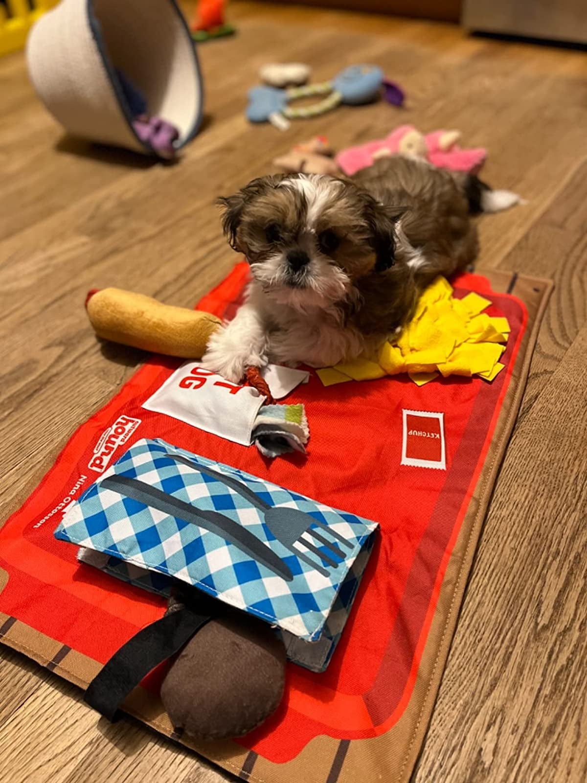 a reviewer's puppy laying on the mat that has fake french fries, hot dog, and silverware