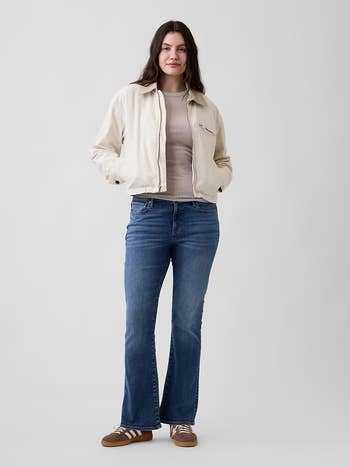 Person wears a casual pick  jacket, airy  sweater, and jeans with brownish  sneakers, suitable for mundane  buying  attire