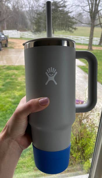 Person holding an insulated tumbler with a handle and straw, featuring a handprint logo; base of the cup is blue