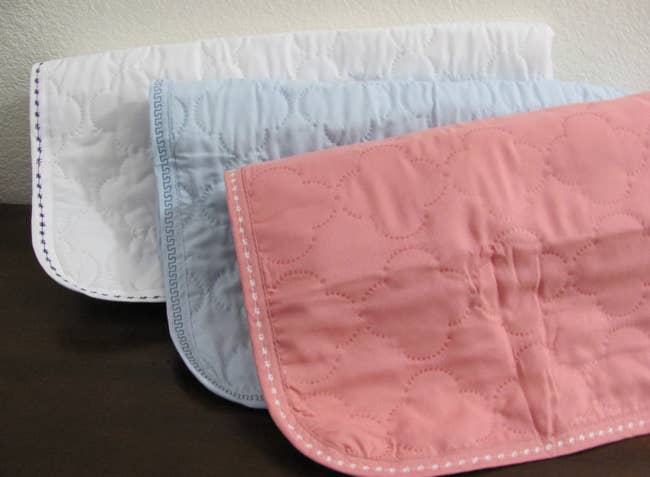 Three bed pads in white, blue, and pink