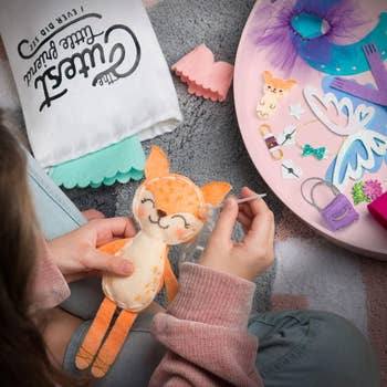 a child model sewing into a fox-shaped plush doll surrounded by other craft materials 