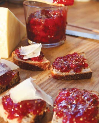 Slices of bread with red jam and cheese on a wooden board, next to a jar of the same jam