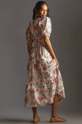 Model poses in a floral print midi dress with puff sleeves and wicker shoes