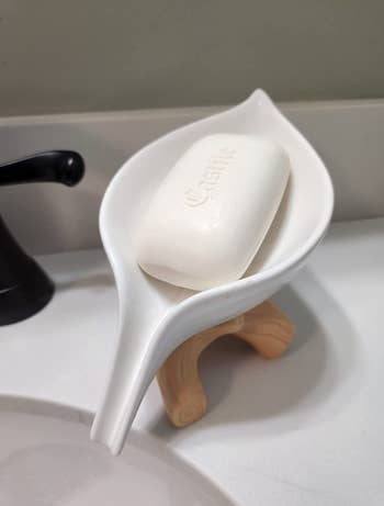 White leaf shaped soap holder elevated by a wooden base 