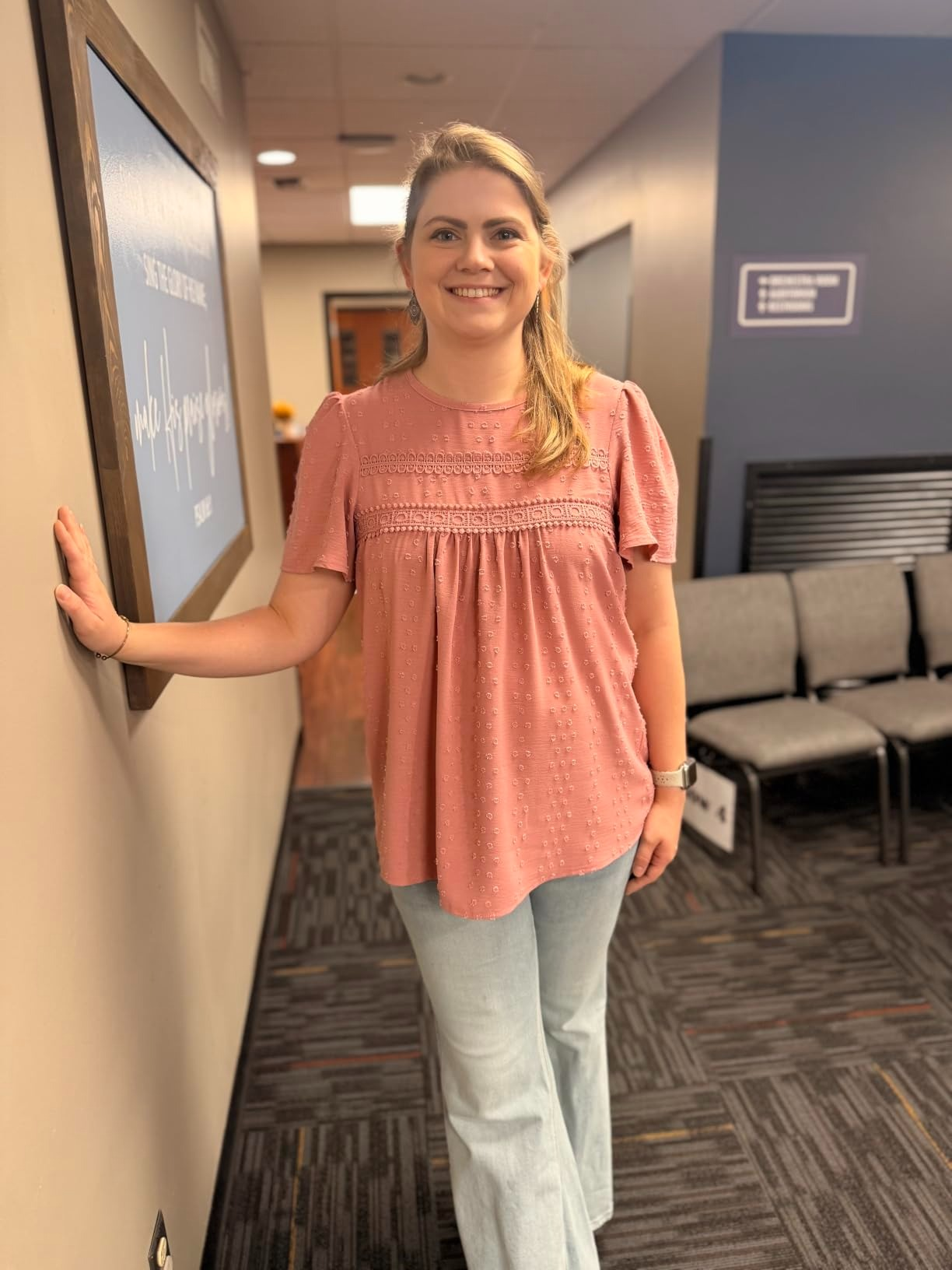 A idiosyncratic   successful  a casual outfit with a decorative apical  and jeans, lasting  indoors, smiling and leaning against a wall