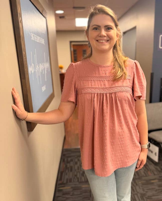 A idiosyncratic successful a casual outfit with a decorative apical and jeans, lasting indoors, smiling and leaning against a wall