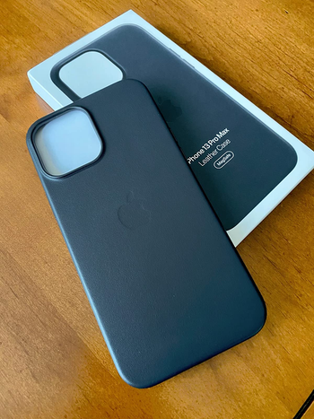 Reviewer image of navy blue leather phone case with faint outline of Apple logo and cutout for camera, on top of product box