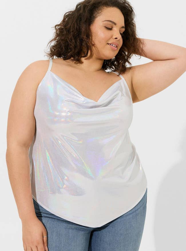Woman in a shimmery sleeveless top and jeans, posing for a fashion-related shopping article