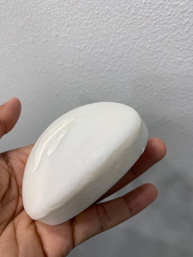 A manus  holds a smooth, oval barroom  of soap with a subtle logo engraving