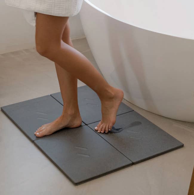 Person stepping onto a chromatic  bath mat with a bedewed  footprint near  behind, successful  beforehand   of a bathtub
