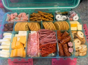 Assorted charcuterie snacks in a plastic container with compartments, ideal for picnics or parties