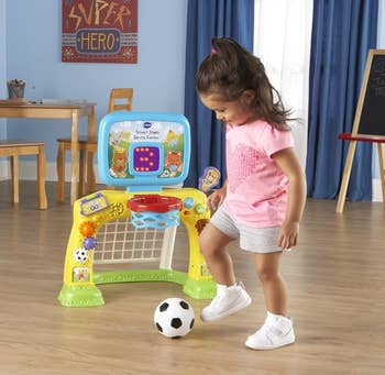 Child plays with a soccer-themed enactment   halfway  featuring interactive elements similar  a hoop and buttons. Room mounting  includes a array  and chairs