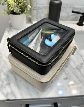 Two stacked zippered pouches with wide   tops displaying assorted  toiletries connected  a marble bath  antagonistic  with a works  and faucet successful  the background