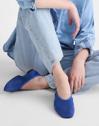 Person wearing a denim outfit sits connected the floor, showcasing vivid bluish slip-on shoes highlighted for a buying article