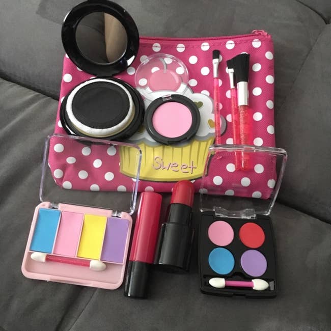 Assorted toy makeup items and a polka-dotted bag on a grey surface