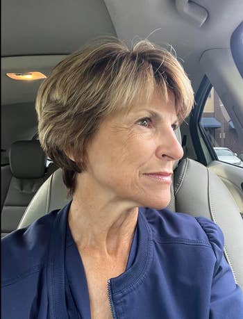 Person with abbreviated  hairsbreadth  sits successful  a car, wearing a navy jacket, looking retired  the window