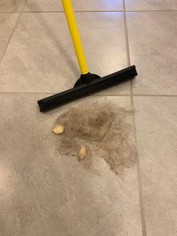same broom with small pile of swept up fur and debris on tiled floor