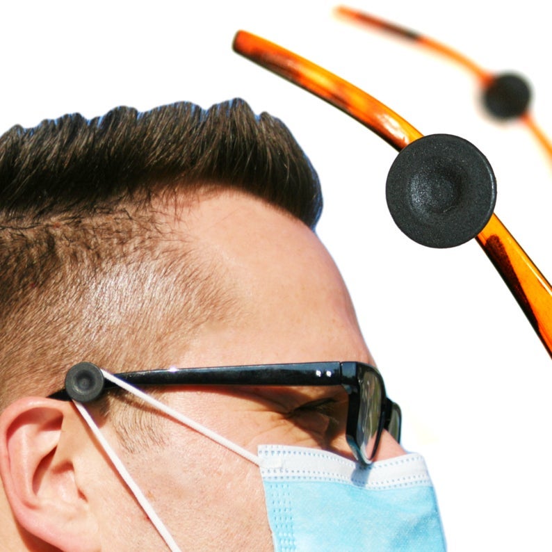 model wearing glasses with the product attached to the side, with their mask hooked around the round hook rather than their ear