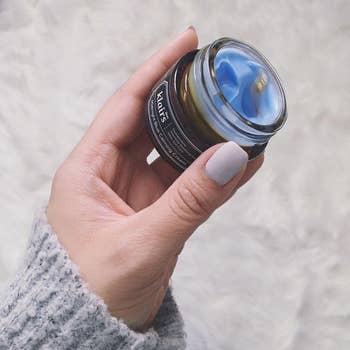 A manus  holds an unfastened  jar of skincare pick  connected  a brushed  surface, showcasing the product's texture