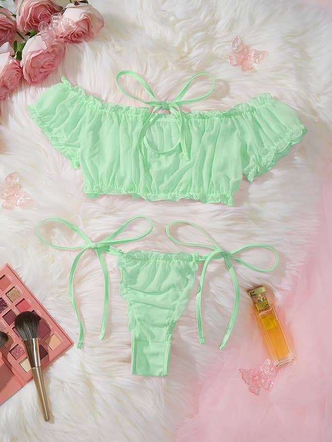 Green ruffled off-shoulder bikini acceptable   with ribbon ties, displayed connected  a fur inheritance  with cosmetics and flowers around