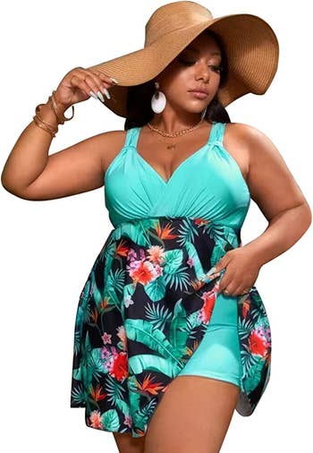 A model wearing the swim dress in teal with floral designs on the skirt