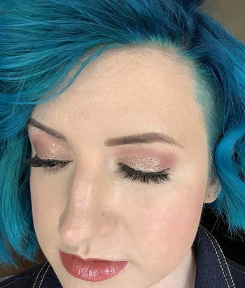 Person with blue hair styled in a textured cut, showcasing glittery eye makeup and glossy lips